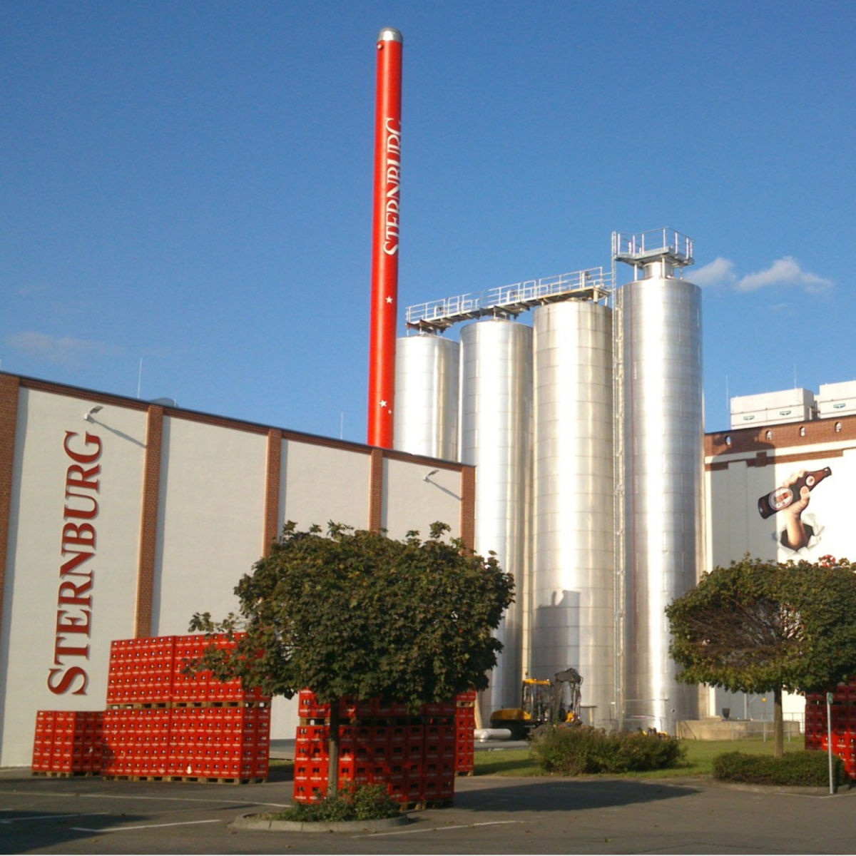 The Sternburg Brewery building. Many stacked beer crates in the foreground, four stainless steel tanks in the background.